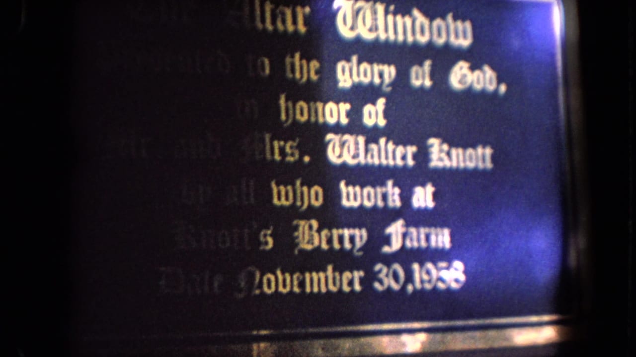 Close view of a dark plaque with Gothic dedication text and bright flare at the edge.