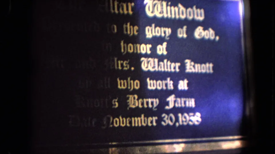 Close-up of the dedication plaque for the altar window, with white Gothic lettering and a bright film flare along the right edge.