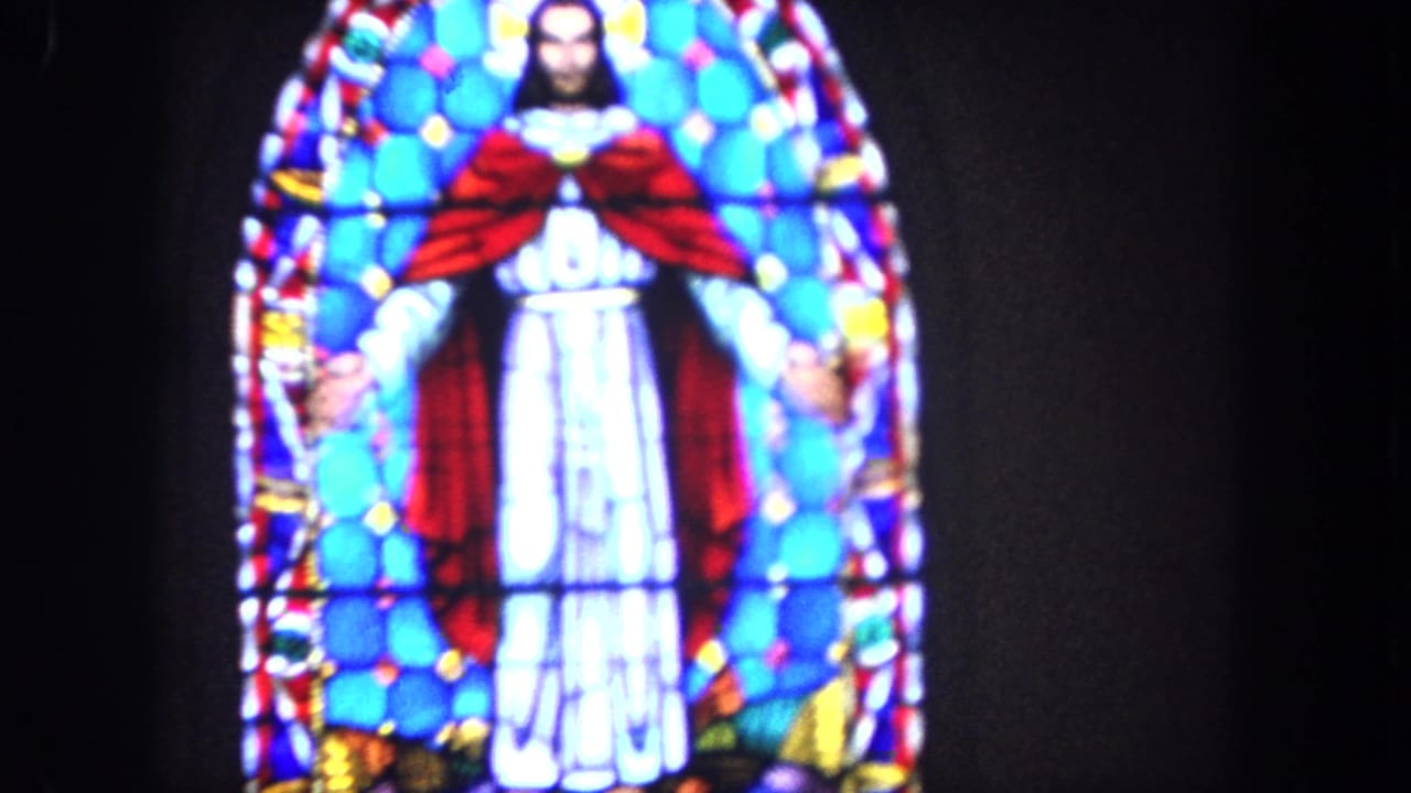 1962 Tijuana home-movie frame showing a stained-glass depiction of Jesus with a red cloak and white robe in a dark church interior.