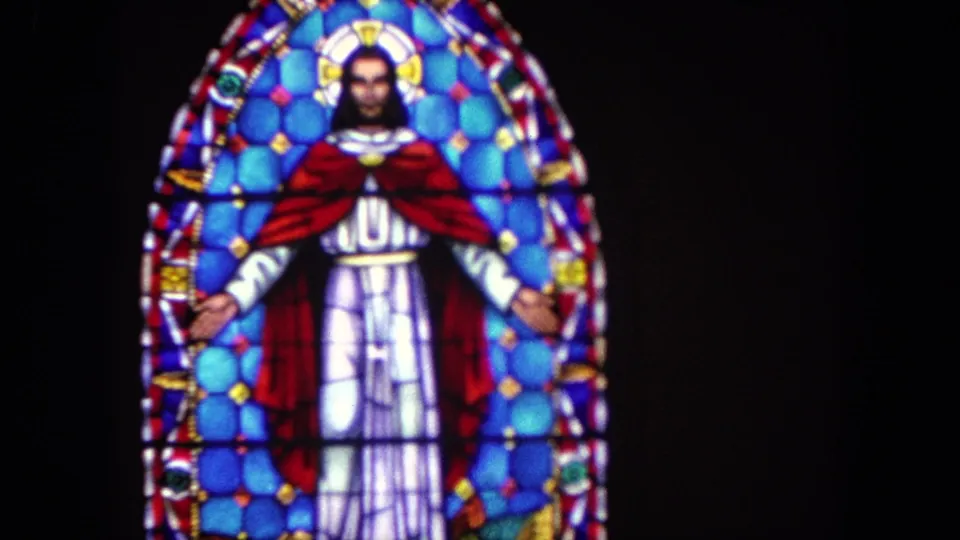 1962 Tijuana frame of an arched stained-glass window depicting Jesus with outstretched arms, red cloak, and blue patterned glass.
