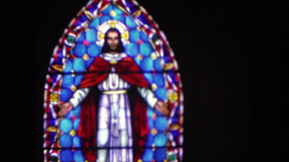 1962 Tijuana home-movie frame with a closer view of the stained-glass Jesus figure, red cloak, white robe, and colored glass border.