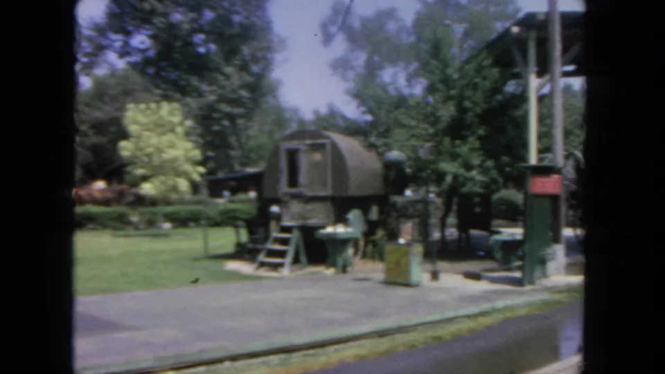 1962 San Diego home-movie frame showing a green dome-shaped trailer, trees, benches, and paved grounds at an outdoor attraction.