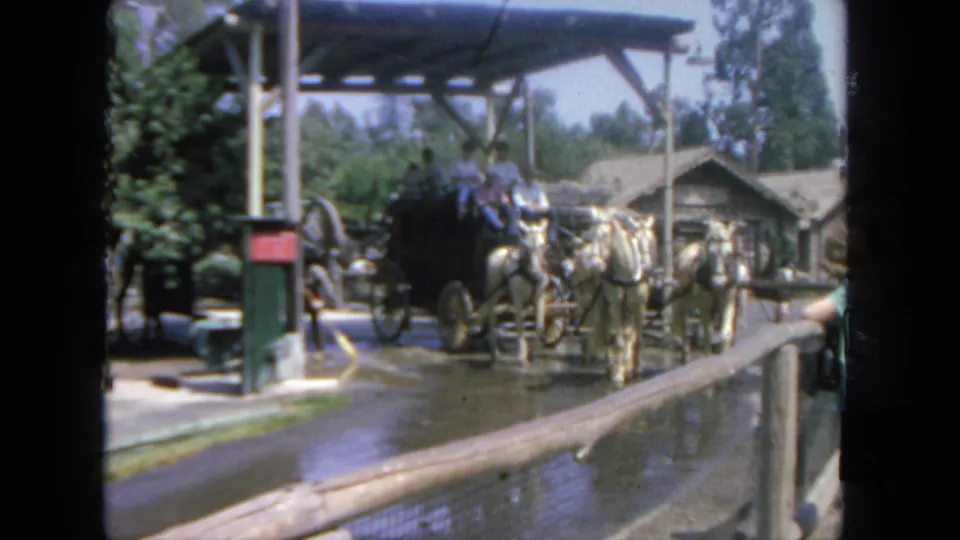 1962 San Diego frame showing riders seated in a black stagecoach behind four white horses at an outdoor attraction.