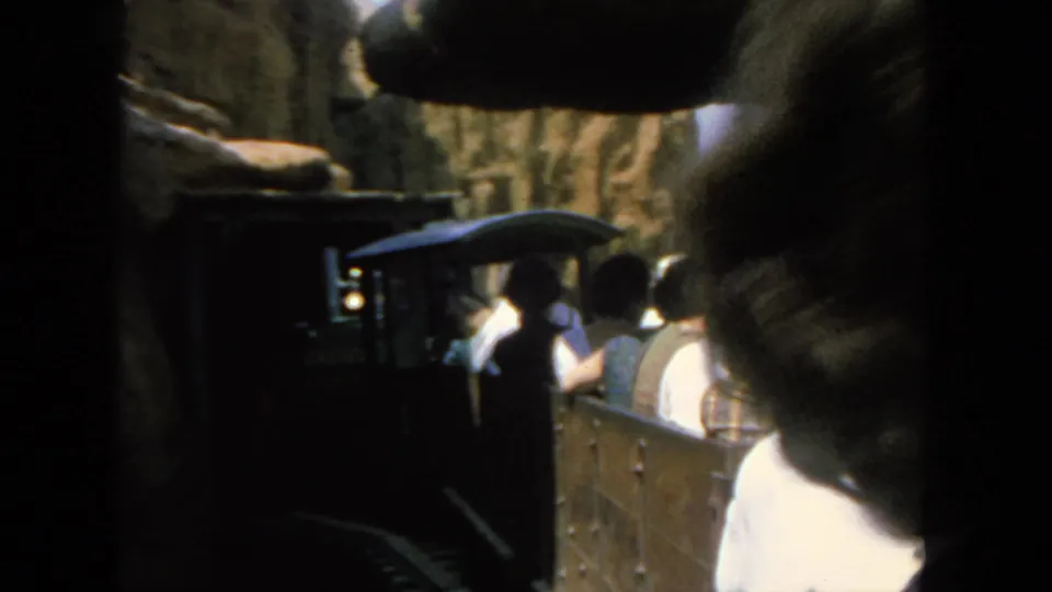 Home-movie view of a tour train approaching a tunnel-like section with passengers seated behind the front car.