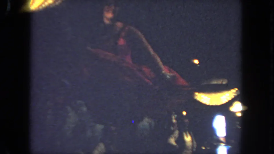In 1962 San Diego home-movie footage, a red-costumed cancan dancer appears mid-kick on a dim stage with bright warm lamps.