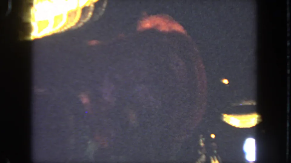 The performer is mostly blurred in motion as the 8mm camera records the dark stage and warm lights during the cancan routine.