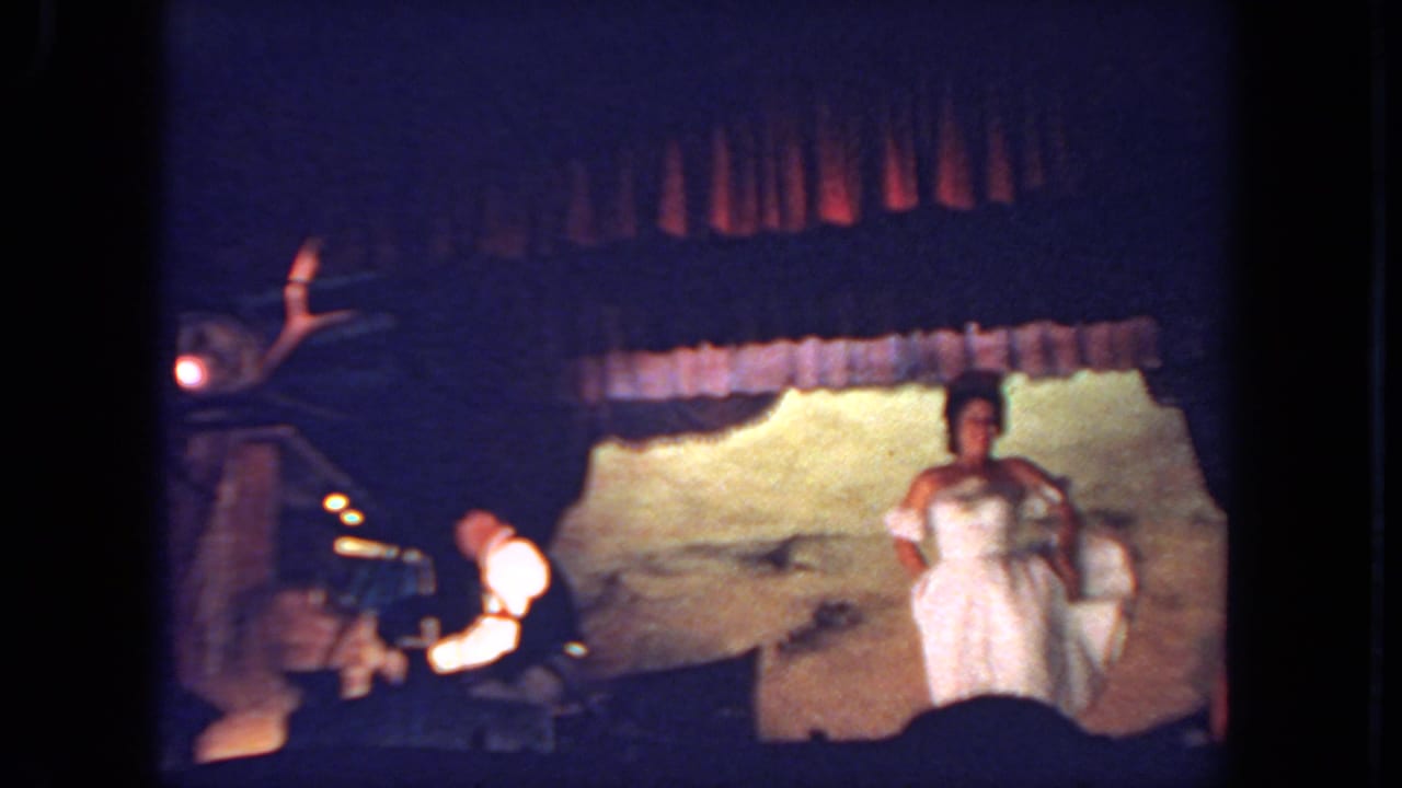 Dancer in a white dress stands onstage near a seated keyboard player.