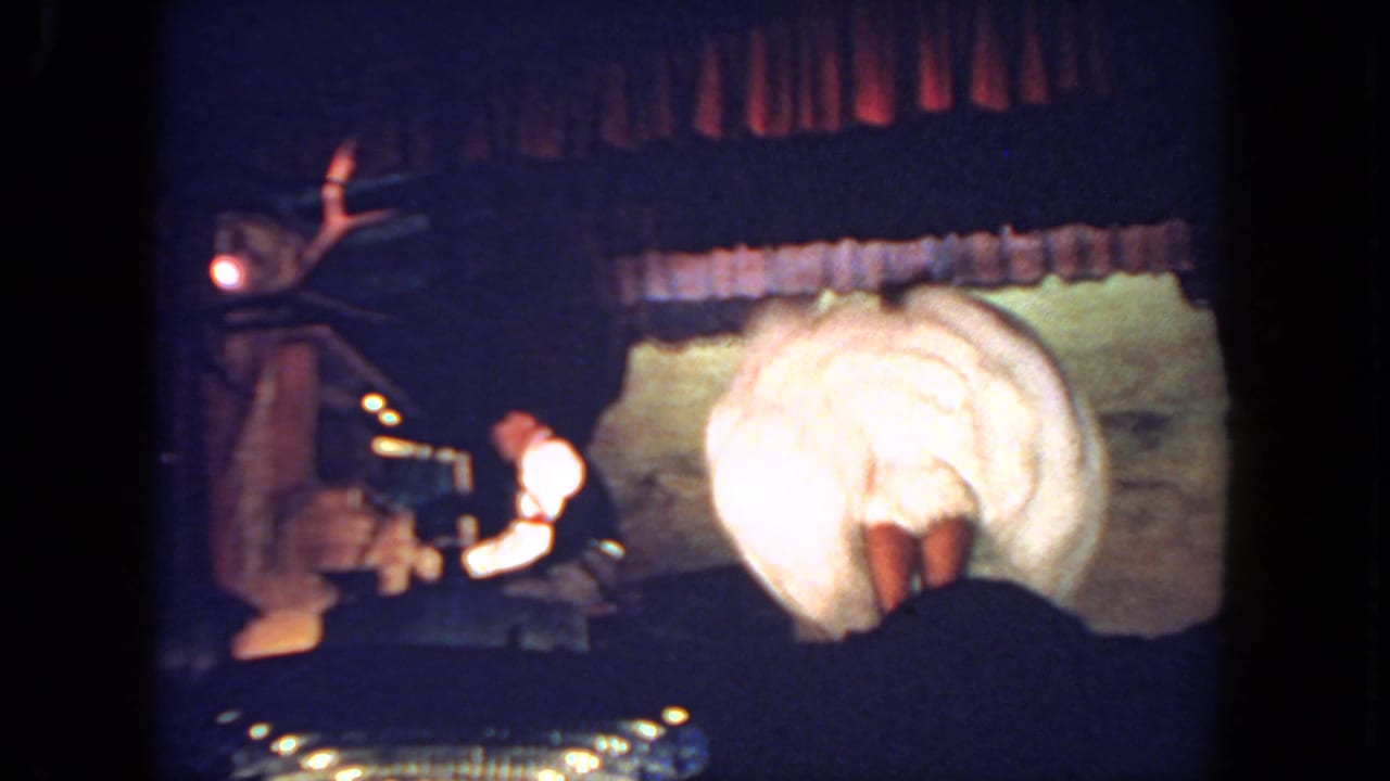 In 1962 San Diego home-movie footage, a cancan-style dancer in a white costume bends under a spotlight while a pianist plays at stage left.
