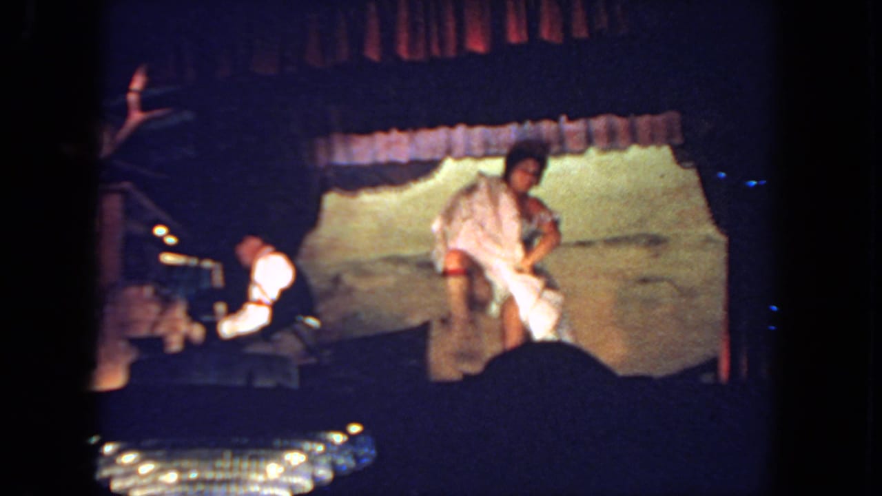 Woman in a light dress stands near center stage while a keyboardist plays at left.