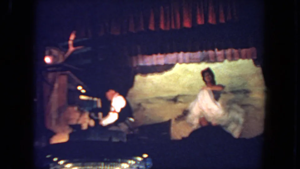 The woman gestures in a light dress under dim stage lighting, with the keyboardist visible at left in the 1962 San Diego clip.