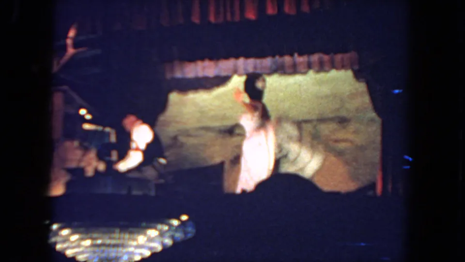1962 San Diego reception frame showing the bride turning in her white gown while the pianist remains seated at the piano.
