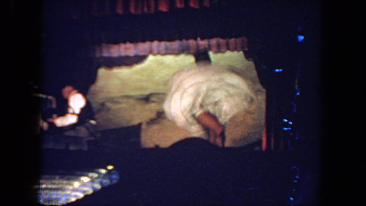 A woman in a white dance costume bends forward on stage while a pianist in a white shirt plays at the side.