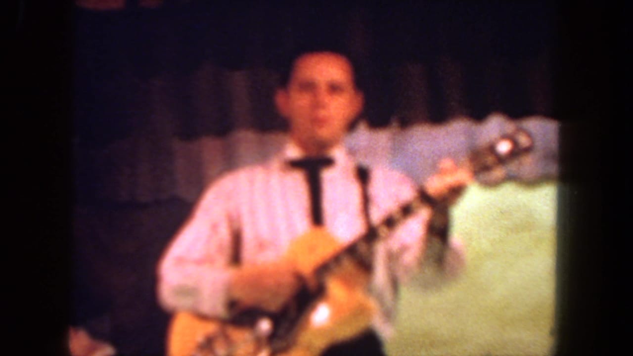 Soft close view of a man holding an electric guitar on stage.