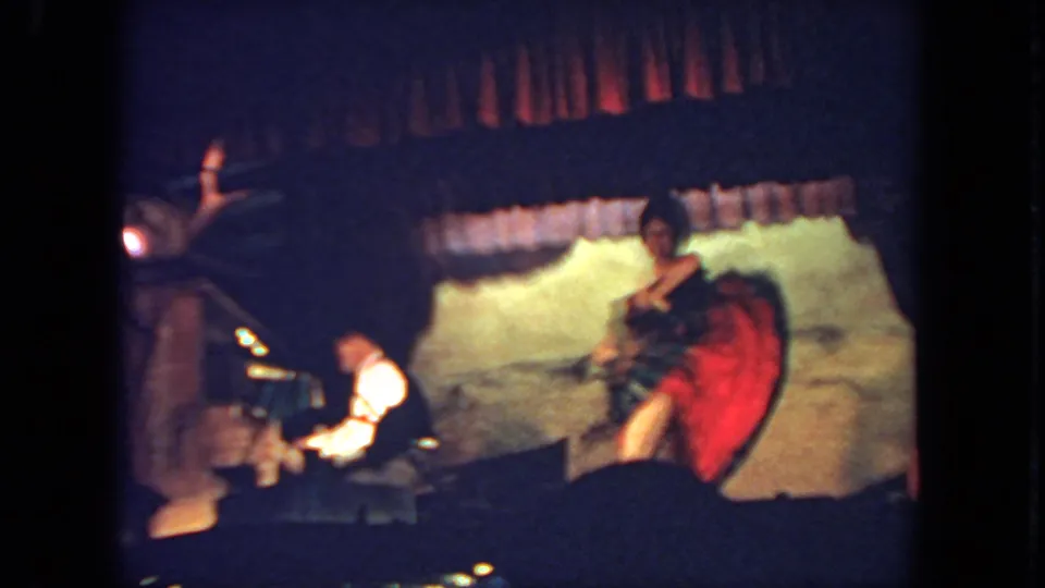 A stage dancer twirls her dress, revealing a red underskirt, as the seated pianist remains at the piano.