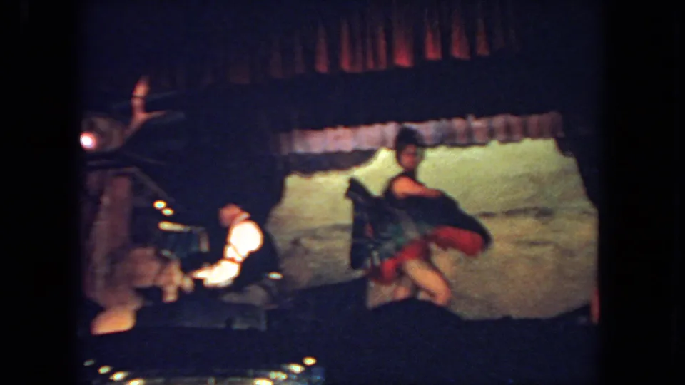 San Diego 1962 8mm frame showing a female dancer on stage with a seated male pianist, red curtain, and painted backdrop.