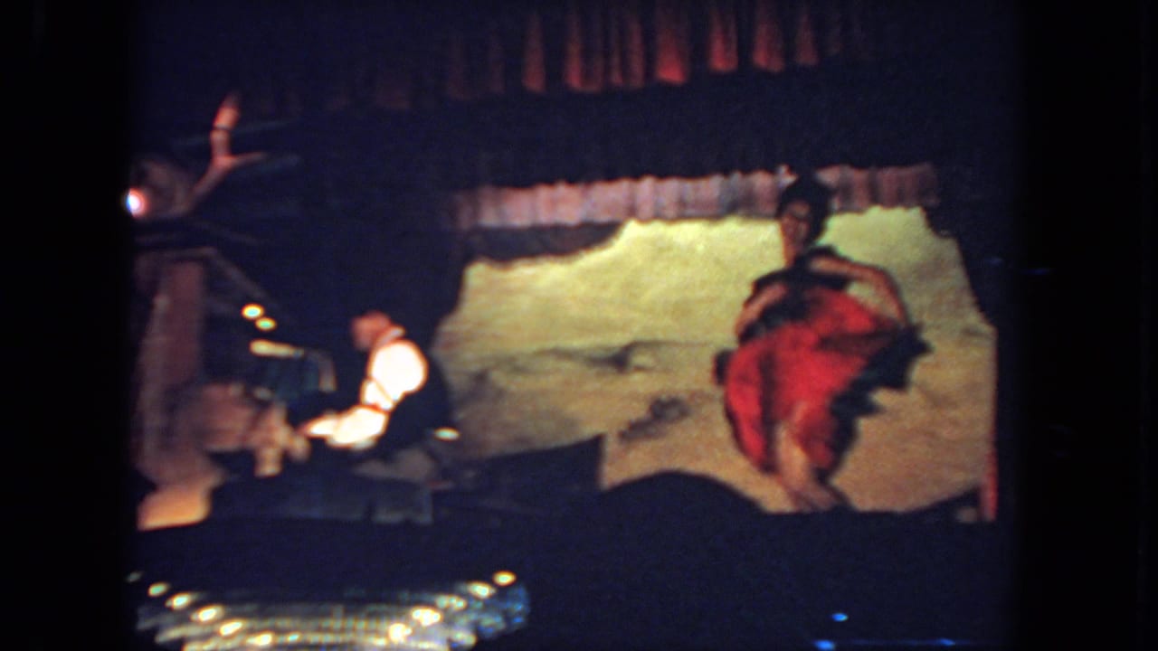 San Diego 1962 8mm frame of a dancer in a red and dark costume performing beside a seated pianist on a small stage.