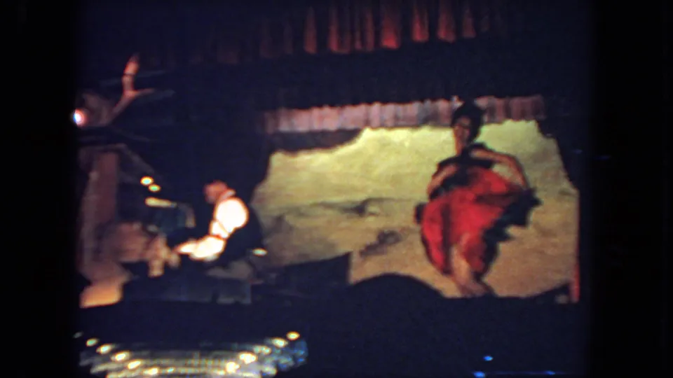 San Diego 1962 8mm frame of a dancer in a red and dark costume performing beside a seated pianist on a small stage.