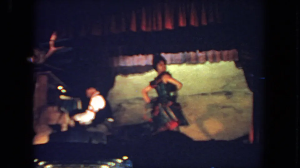 The dancer appears in a darker red skirt near the end of the 1962 San Diego stage clip, with piano accompaniment and audience silhouettes visible.