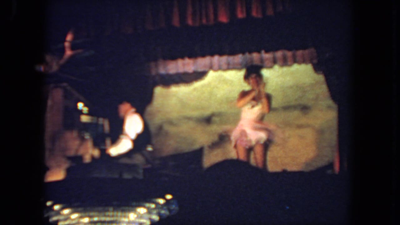 A woman in a pale pink dress performs on a small San Diego stage in 1962, with a pianist seated at the left.