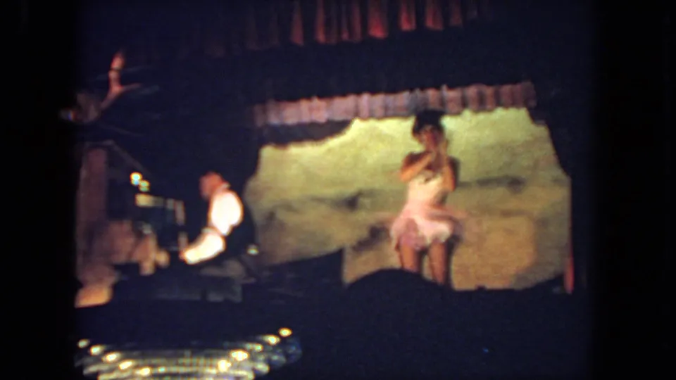A woman in a pale pink dress performs on a small San Diego stage in 1962, with a pianist seated at the left.