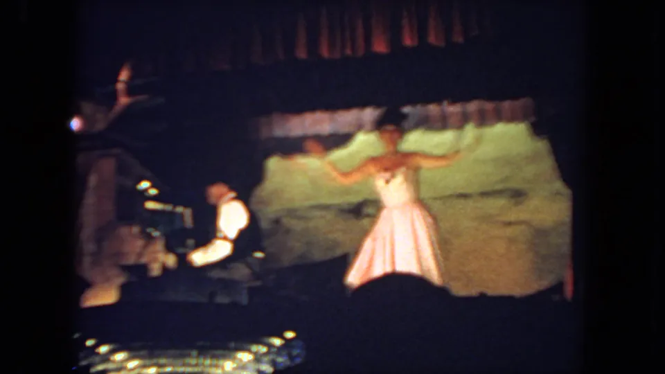 The performer extends her arms during a 1962 San Diego stage dance, filmed from the audience with the pianist at left.