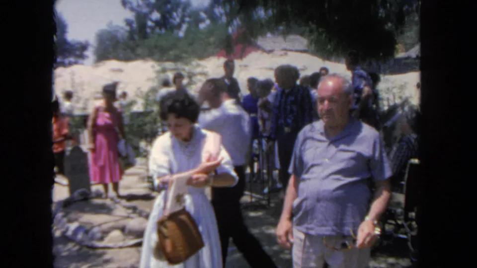 1962 San Diego frame showing tourists on a path, with a woman reading a booklet and a man beside her amid a busy attraction crowd.