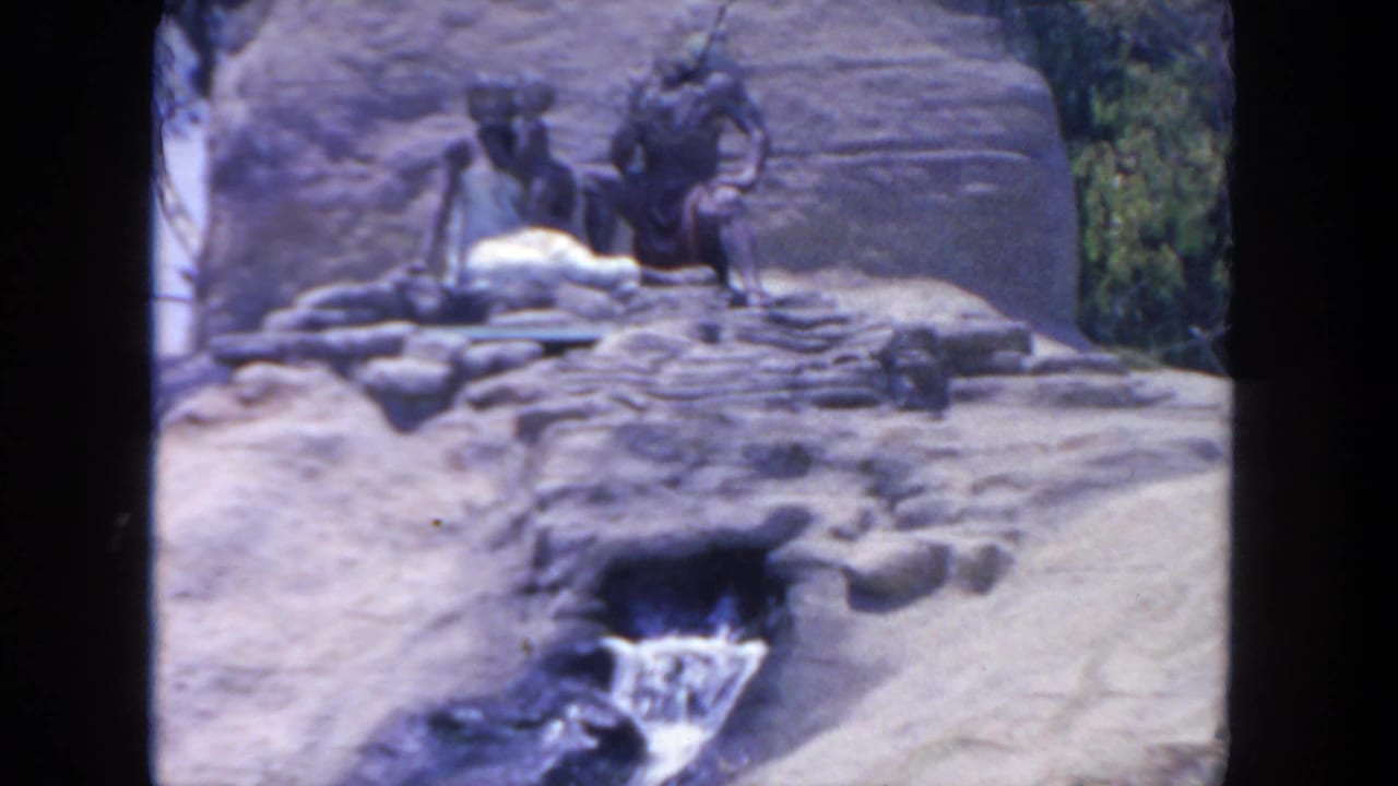 Rocky zoo exhibit with seated statues above a small waterfall.