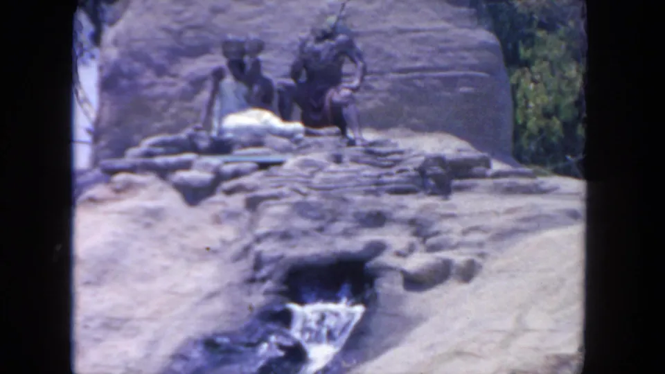 1962 San Diego zoo exhibit view with human-like statues on artificial rocks above a small waterfall and greenery.