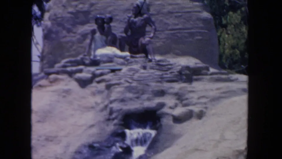 1962 San Diego zoo footage frame with human-like statues on rockwork and a small cascade running into a lower pool.