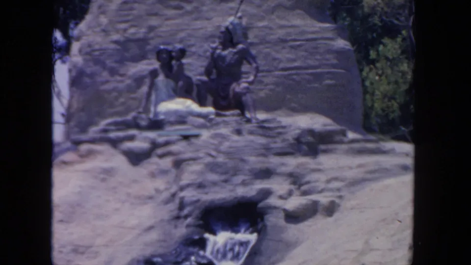 End frame from a 1962 San Diego zoo exhibit shot, showing seated statues, artificial rocks, greenery, and a small waterfall.