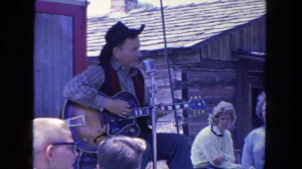 The final frame keeps the 1962 San Diego performer, microphone, electric guitar, and rustic outdoor stage in view from the audience.