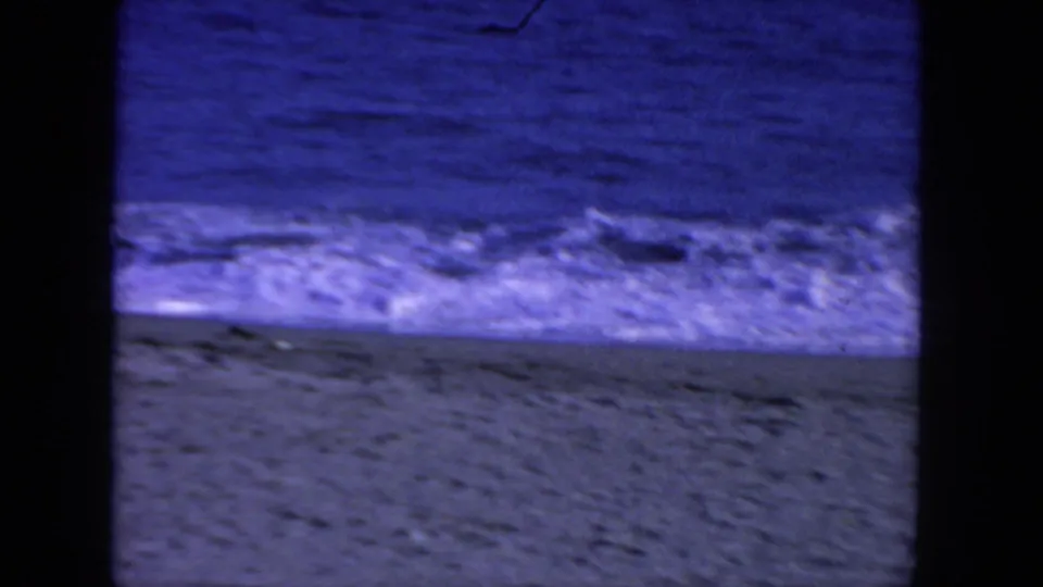 8mm home-movie frame from San Diego in 1962 showing foamy surf breaking along a sandy beach with open water beyond.