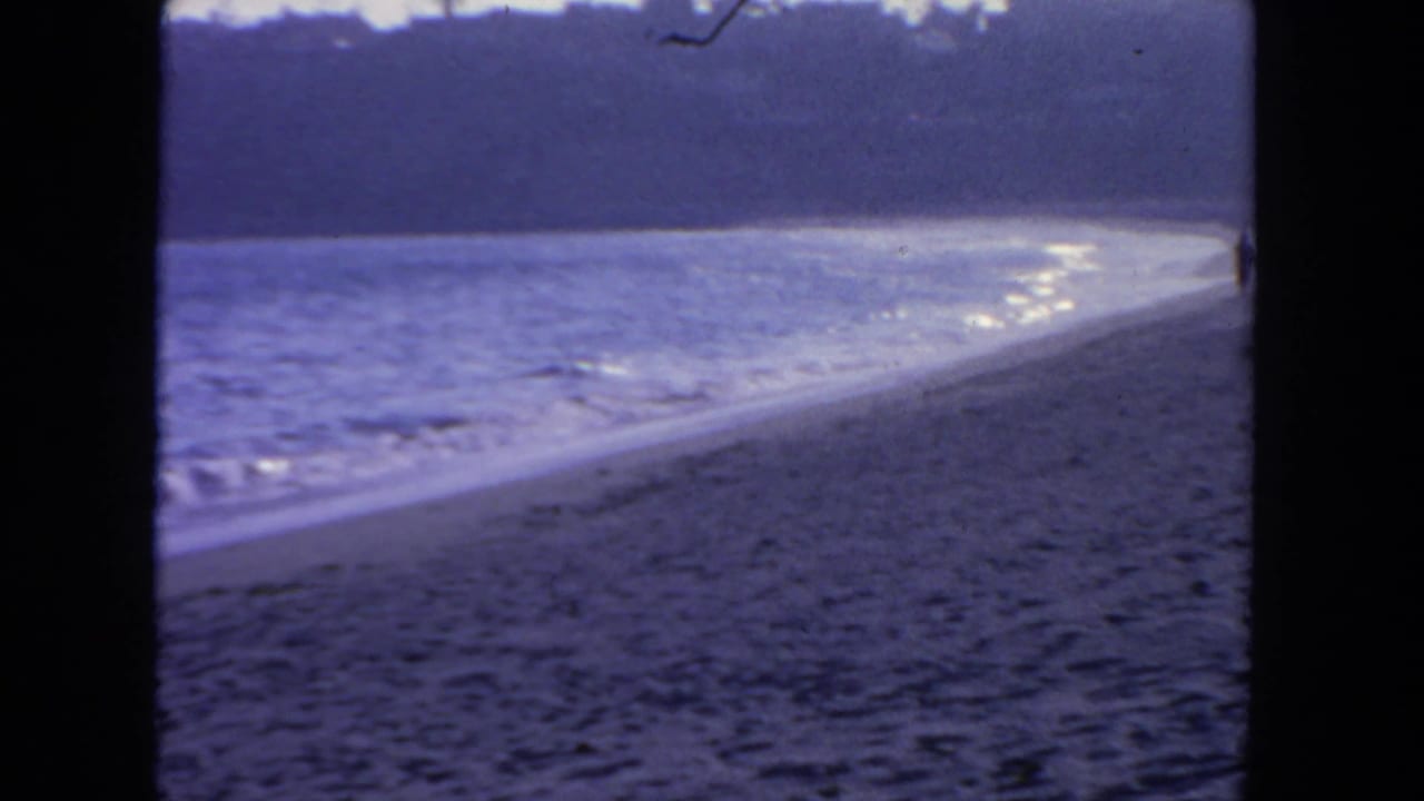 Waves wash onto a sandy beach with a dark hillside across the water.