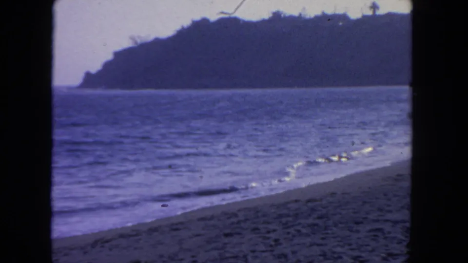 1962 San Diego 8mm view of low waves, wet sand, and a silhouetted coastal hill across the water.