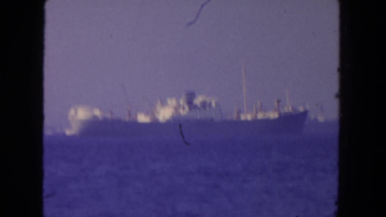 1962 San Diego 8mm frame showing a large offshore ship through haze, with a soft purple cast and visible film wear.