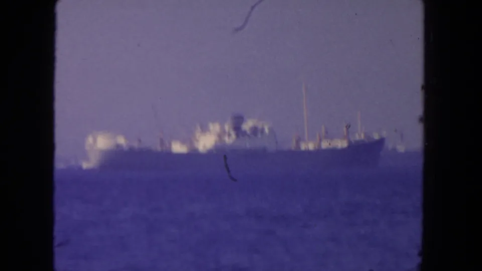 1962 San Diego 8mm frame showing a large offshore ship through haze, with a soft purple cast and visible film wear.