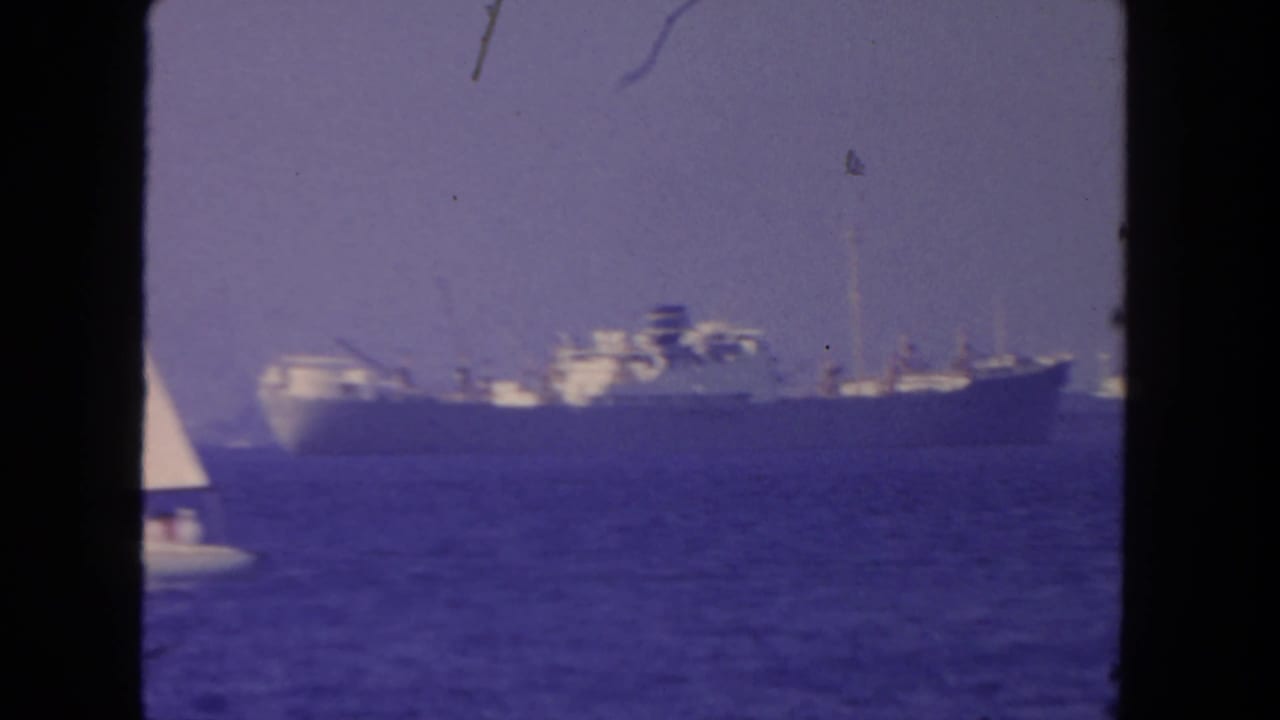 Distant large ship on blue water with part of a sailboat at left.