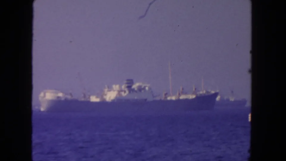 A distant anchored ship remains framed against hazy sky and rippled water in this 1962 San Diego home-movie shot.