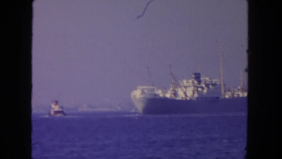 1962 San Diego-area 8mm frame showing a distant steamer on open water with a smaller boat nearby.