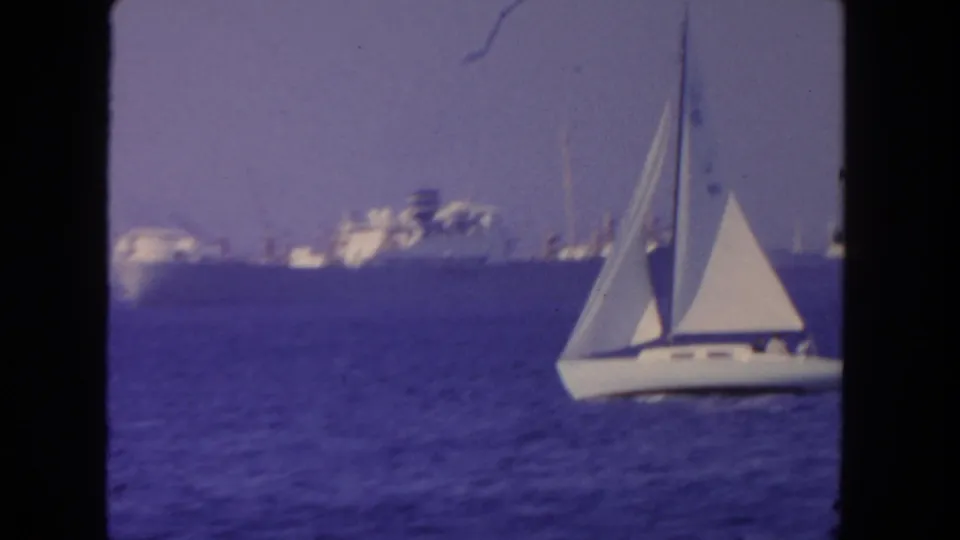 A white sailboat passes in front of a distant steamer on San Diego-area ocean water in 1962 footage.