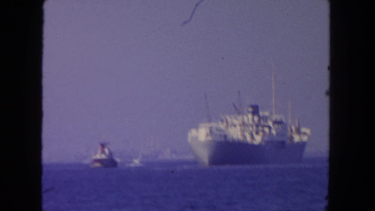 Large cargo ship on the ocean with a small tugboat nearby under a hazy sky.