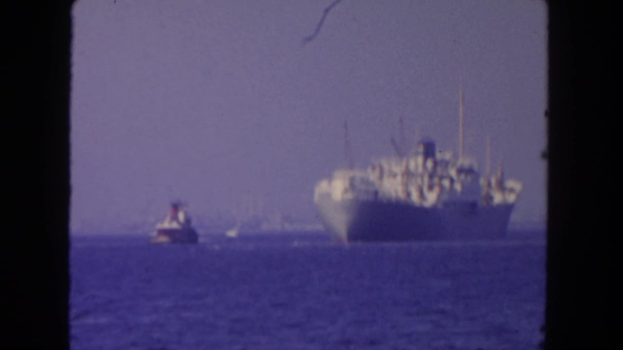 Cargo ship and tugboat travel across open water with the ship closer to frame right.