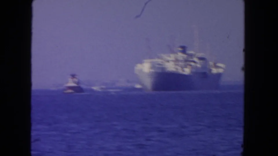 Soft 1962 San Diego home-movie frame showing a distant large vessel and tugboat moving across blue ocean.