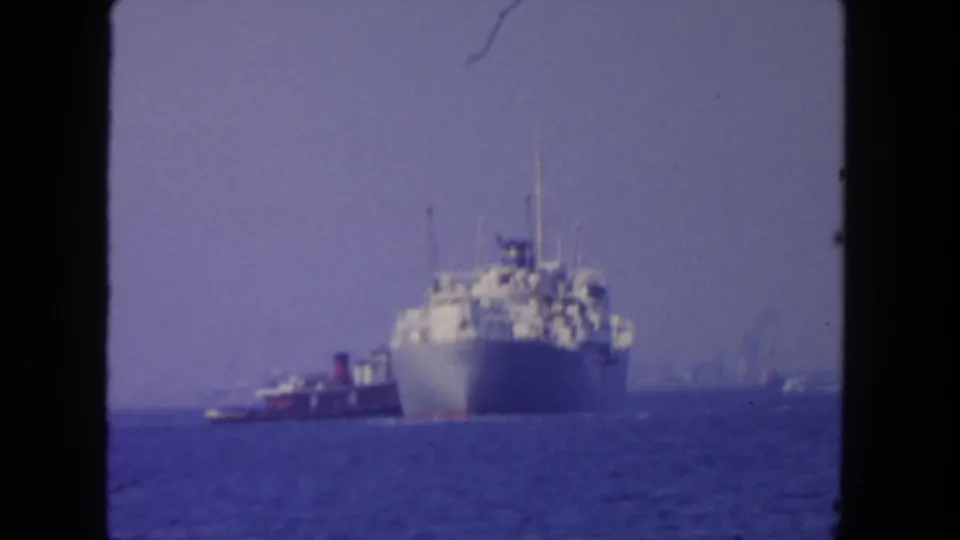 Likely San Diego harbor view from 1962, with a distant passenger ship and tugboat framed by soft 8mm color and haze.
