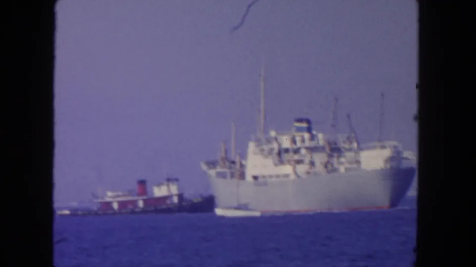1962 San Diego home-movie frame of a large freighter and tugboat moving across blue water.