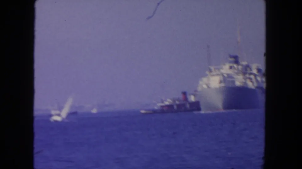 1962 San Diego 8mm frame with a cargo ship, tugboat, and a small white sail visible across the water.