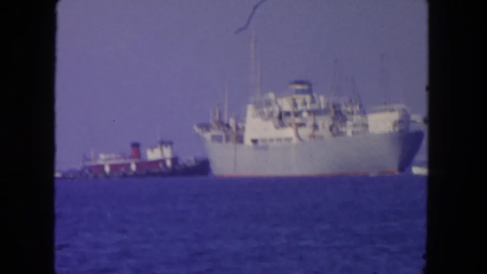 A large white transport-like vessel and a smaller support boat float offshore in 1962 San Diego-area 8mm footage.