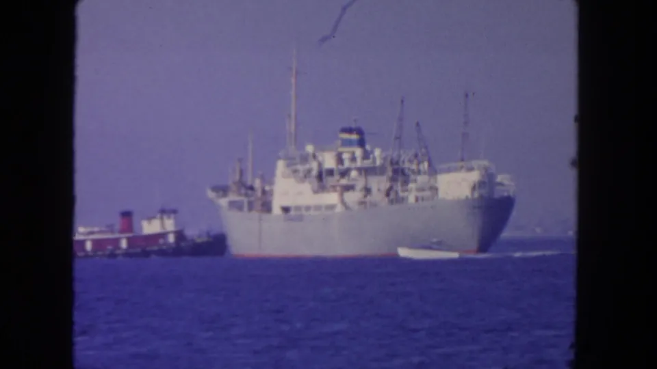 A large white vessel, smaller craft, and calm blue water appear in a 1962 San Diego naval harbor view.