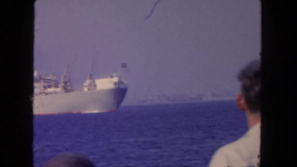 1962 San Diego coastal frame with a cargo ship in the distance and a man viewed from behind near the right edge.