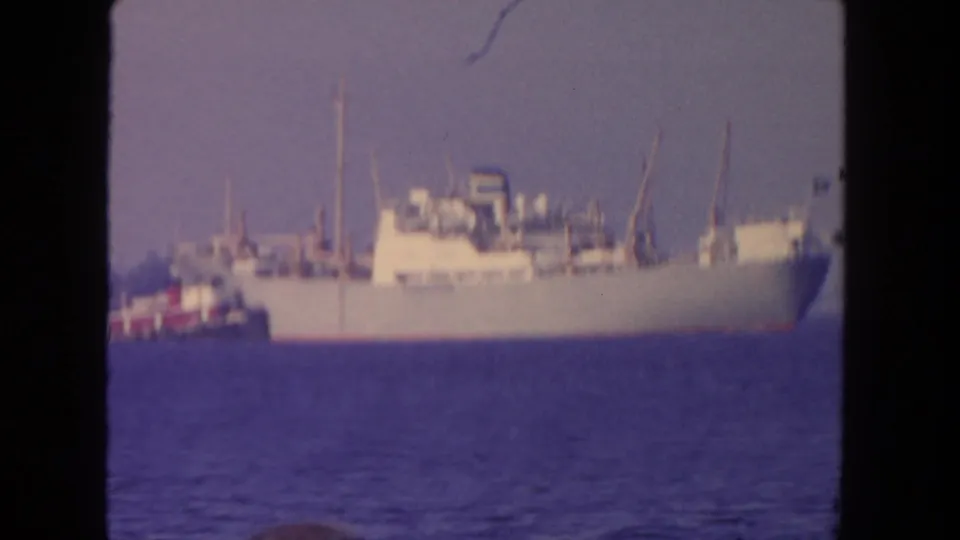 Soft 8mm frame from 1962 San Diego showing a white cargo ship moving through harbor water with a tugboat partly visible.